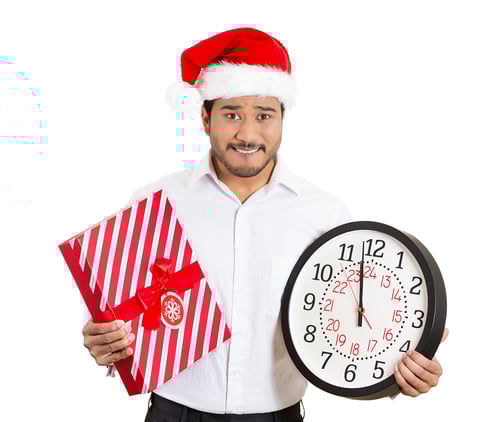 Closeup portrait of worried young man wearing red santa claus hat, holding clock and gift in hands, isolated on white background. Negative emotion facial expression. Last minute christmas shopping-1
